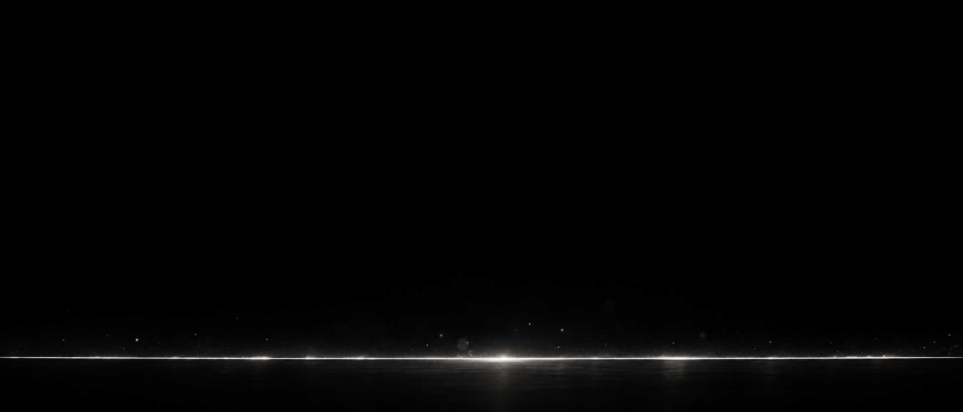 A panoramic nearly black image with one long extremely fine white slit near the bottom, a few tiny silver sparkles just above it.