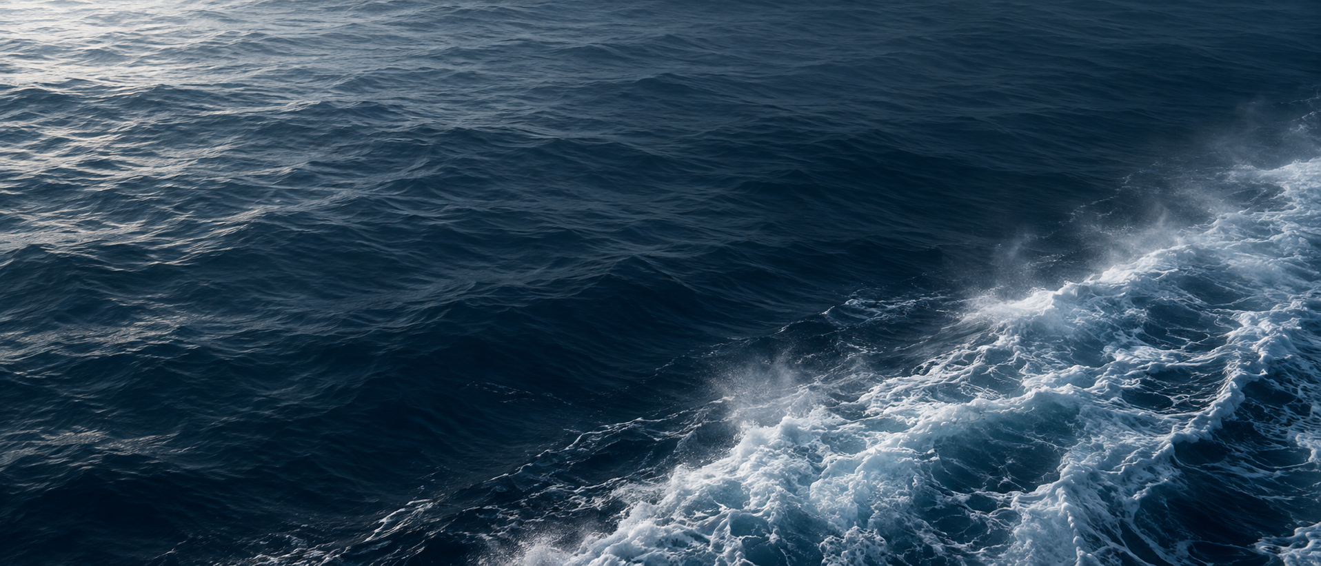 Minimal almost abstract macro ocean surface in ink blue with one soft diagonal trail of dissolving ship wake along the bottom right, upper and left areas calm, no ship visible.