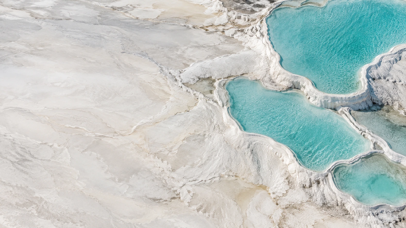 Aerial view of a few naturally formed shallow pale turquoise mineral pools in white travertine, irregular organic edges.