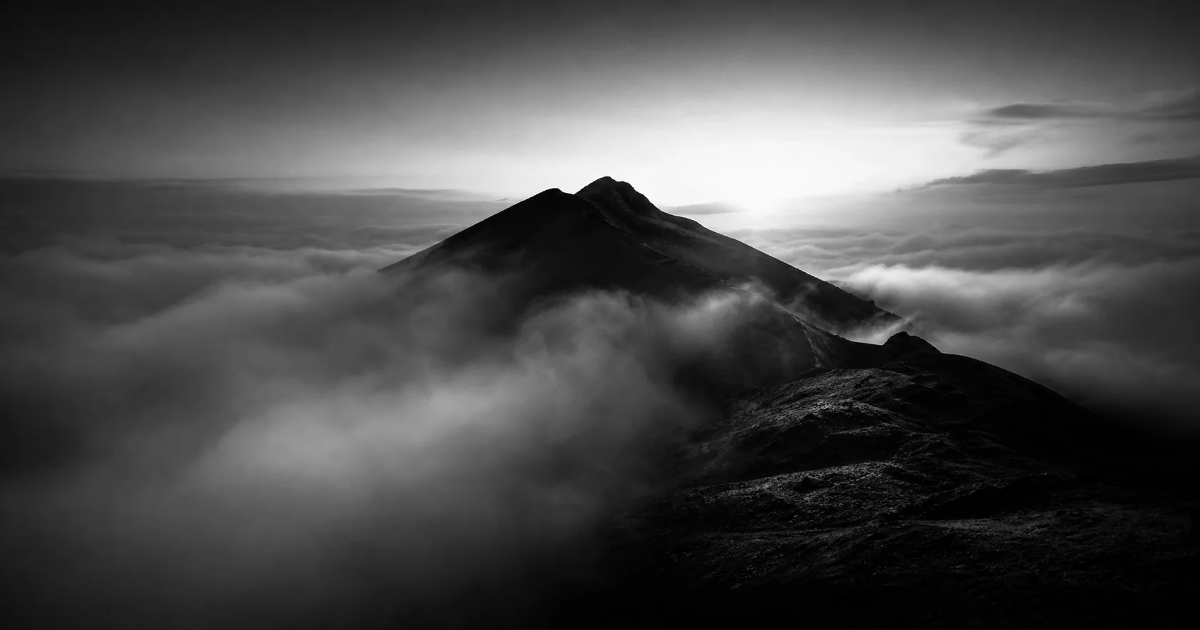 A rugged alpine ridge above a sea of clouds in cool evening shadows.