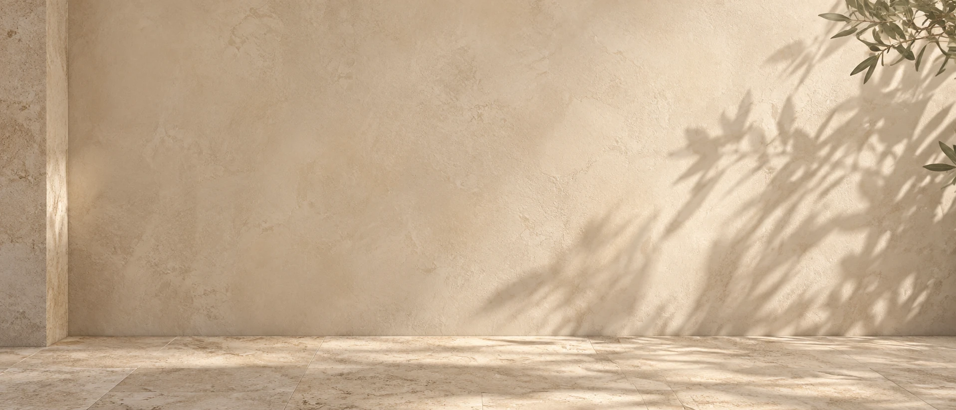Low-detail close-up of warm plaster wall with large soft olive leaf shadows drifting across lower right, light stone floor along bottom edge, quiet text background.